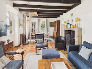 A living room with a fireplace, a wooden staircase, and a dining area.