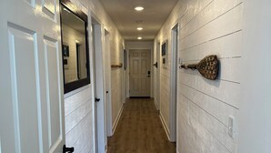 A narrow hallway with white walls and wooden flooring, leading to a door at the end.