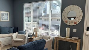 A modern living room with a large window, a round mirror with seashells, and a wooden coffee table.