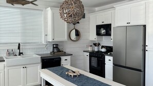 A modern kitchen with white cabinetry, a stainless steel refrigerator, a wooden bench, and a hanging light fixture.