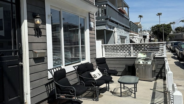 A patio with outdoor seating, a grill, and a view of a residential street.