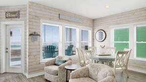 A room with a view of the beach, wooden walls, a dining area with chairs and a table, and a sign that says "Gulf Shores." - Gulf Front Luxury | Private Pool and Elevator (Gulf Shores)