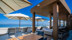 Una terraza de madera con mobiliario exterior, sombrillas y vista al océano.