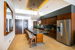 A modern kitchen with a central island, wooden cabinets, stainless steel appliances, and pendant lighting.