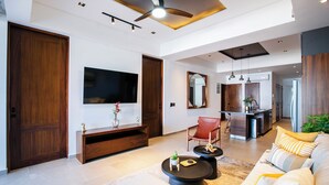 Una sala de estar moderna con un televisor de pantalla plana grande, muebles de madera, un sillón rojo, un sofá con cojines a rayas y un ventilador de techo.