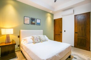 A bedroom with a bed, a nightstand, a lamp, and a door. - Amapas Oasis | Pool & Private BBQ (Puerto Vallarta)