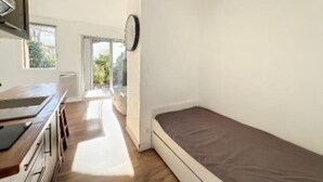A small, bright room with a kitchenette, a single bed, and a view of the outdoors.