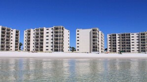 Ett hotell vid stranden med flera vita byggnader, klarblå himmel och en sandstrand.