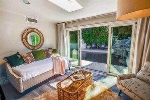 A modern living room with a sofa, a wicker coffee table, and a view through large glass doors to an outdoor area. - Modern Desert Home | Heated Pool (Scottsdale)