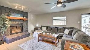 A living room with a stone fireplace, a ceiling fan, a grey sofa, and a coffee table. - SunRay Stay ~ Heated Pool, Putting Green, & Patio (Safety Harbor)