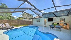A covered outdoor swimming pool with a patio area, including lounge chairs and a bar. - SunRay Stay ~ Heated Pool, Putting Green, & Patio (Safety Harbor)