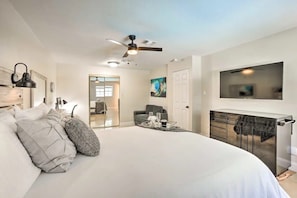 Un dormitorio moderno con una cama grande, un ventilador de techo, un televisor montado en la pared y una puerta de cristal que da a otra habitación.
