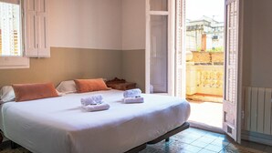 Una camera d'albergo con un letto, cuscini, un comodino e una porta aperta su un balcone.