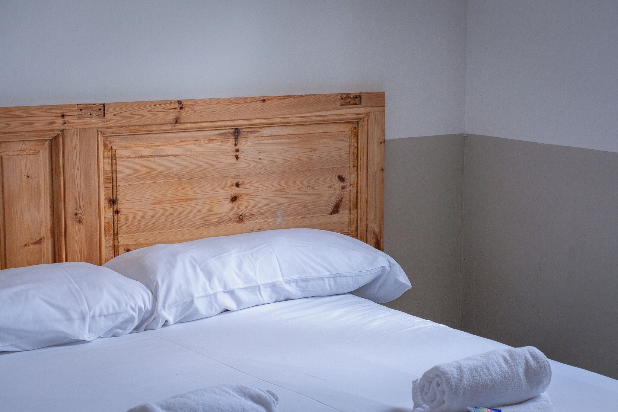 A neatly made bed with white linens and pillows, a wooden headboard, and a folded towel on the bed.