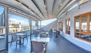An outdoor terrace with tables and chairs, a view of the city, and a covered area with lights. - Cihangir Palace Hotel (Istanbul)