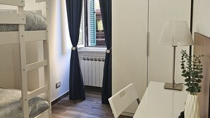 Ett sovrum med en våningssäng, ett skrivbord med en lampa och ett fönster med gardiner.