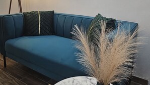 Ett rum med en blå soffa, ett runt bord i marmor med en vas på, och tre inramade konstverk på väggen.
