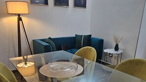 Ett modernt matområde med ett glasbord, gula stolar, en blå soffa och konst på väggen.