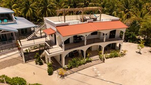 A multi-story building with balconies, a covered patio, and a sandy ground area. - Paradise Inn Placencia - Toucan Suite on the beach (Placencia)