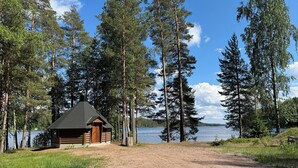 Une cabane dotée d’un toit conique, entourée de grands arbres et bordée par un lac.