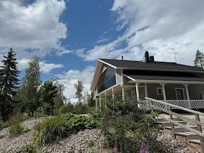 A house with a porch, a staircase, and a garden with various plants and a small pond. - Matikkala Cottages (Ruokolahti)