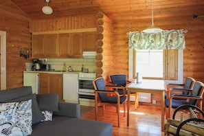 A cozy cabin interior with wooden walls, a dining area with chairs, a sofa, and a kitchen with wooden cabinets and appliances. - Matikkala Cottages (Ruokolahti)