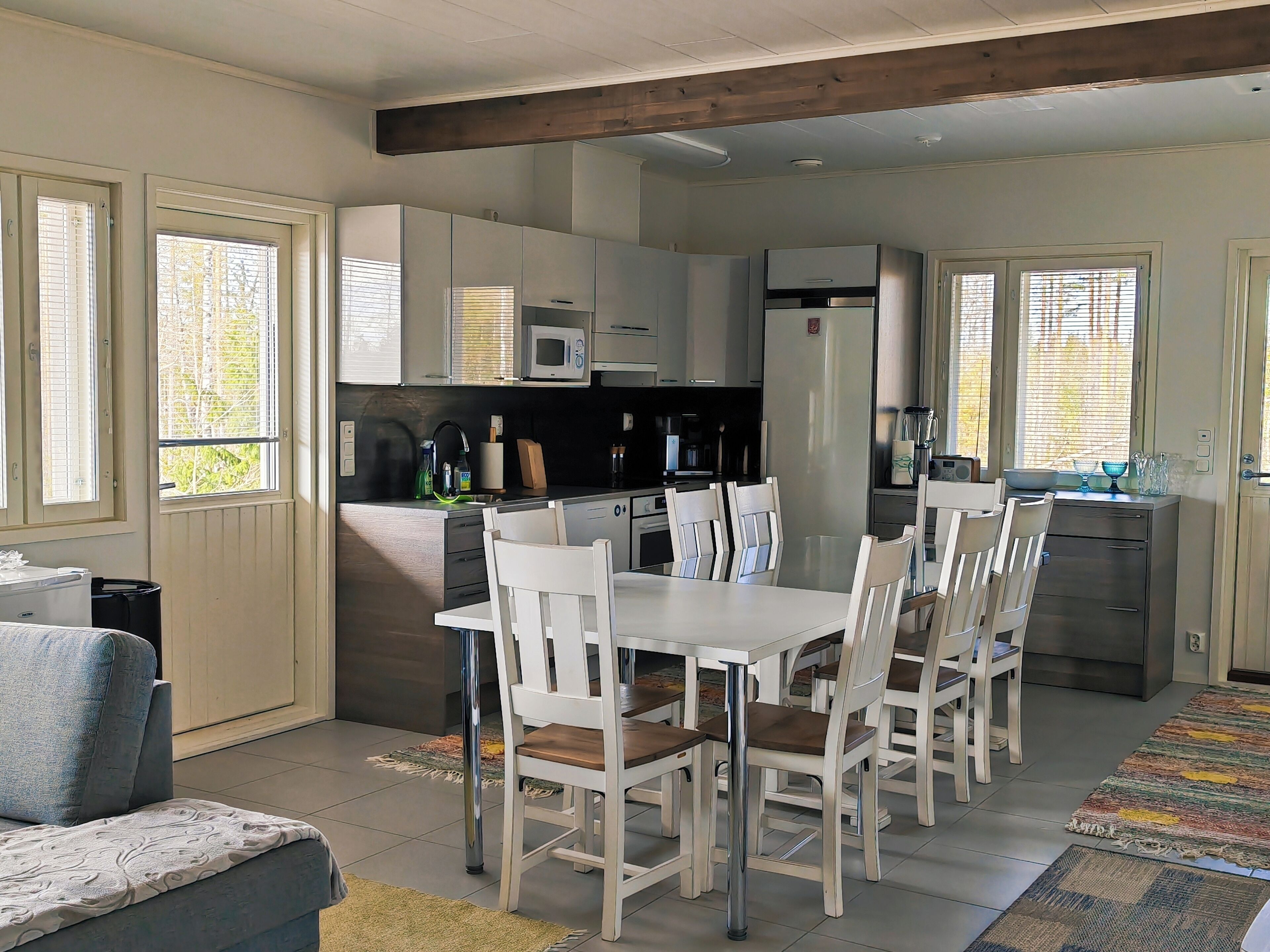 A modern kitchen with white cabinets, a dining table with chairs, and a sofa.