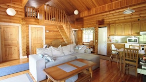 L’intérieur chaleureux d’un chalet avec un escalier en bois, un canapé, une table à manger et un coin cuisine.