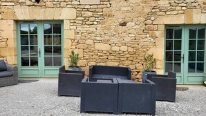 Ein Gebäude aus Stein mit grünen Türen und einer Terrasse mit Korbmöbeln.
