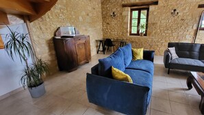 Ein Zimmer mit steinernen Wänden, einem blauen Sofa, einem grauen Sofa und einem Holzschrank.