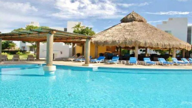 A swimming pool with lounge chairs and a thatched-roof structure.