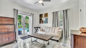 Un salon moderne avec un canapé, une table basse en bois, un ventilateur de plafond et une vue sur une piscine.