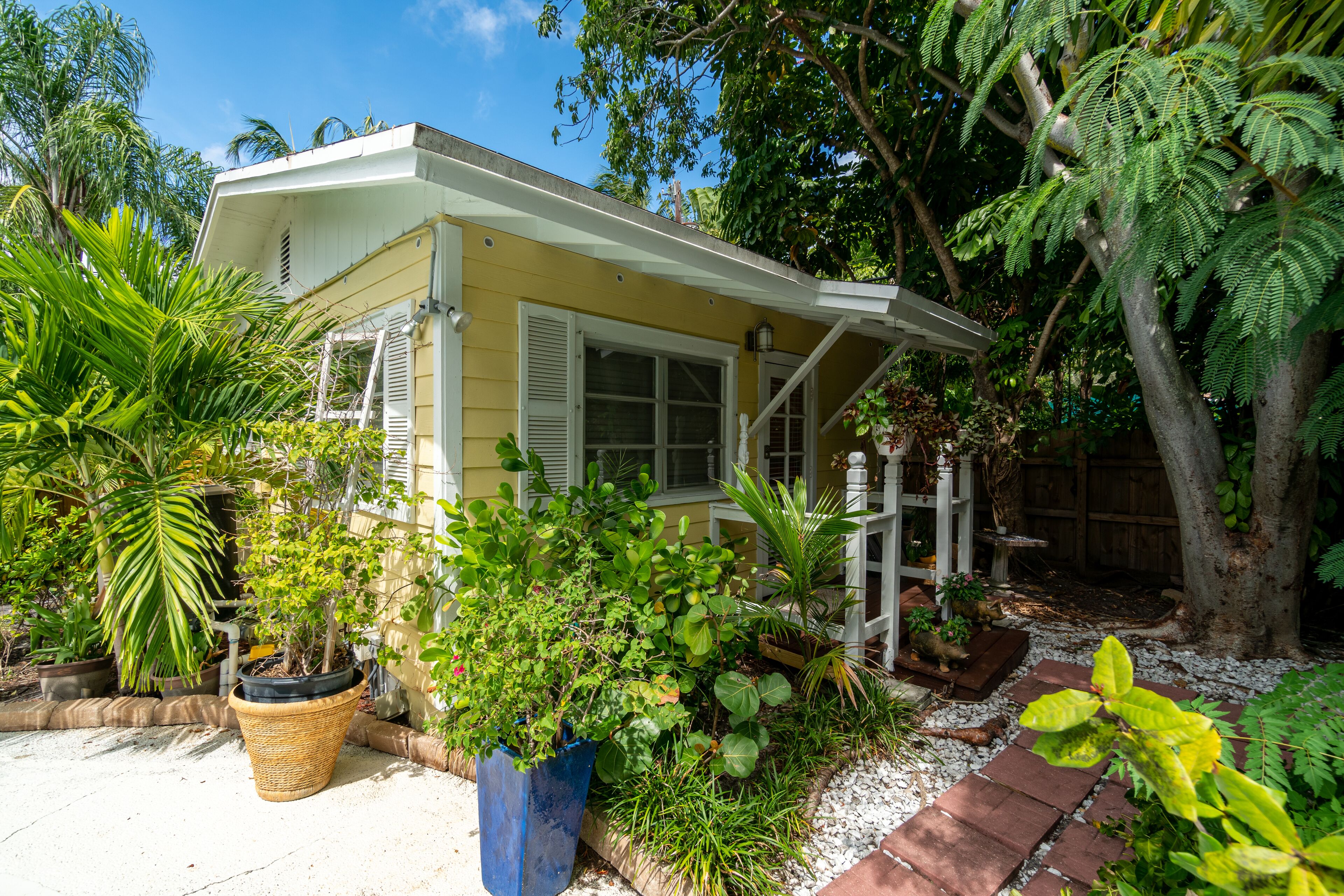 A small house with a porch, surrounded by various potted plants and trees.