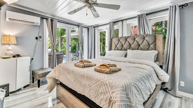 Une chambre à coucher avec un lit, un ventilateur de plafond, une table de chevet, une lampe et une vue sur l’extérieur.