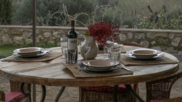 Une table ronde en bois, dressée pour le dîner, avec vue sur un château perché sur une colline.
