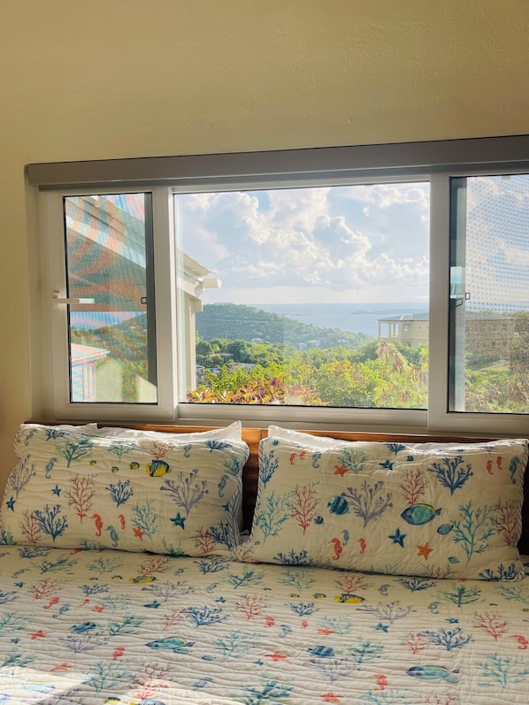 Una camera da letto con un'ampia finestra, un letto con copriletto floreale e vista sul paesaggio costiero.