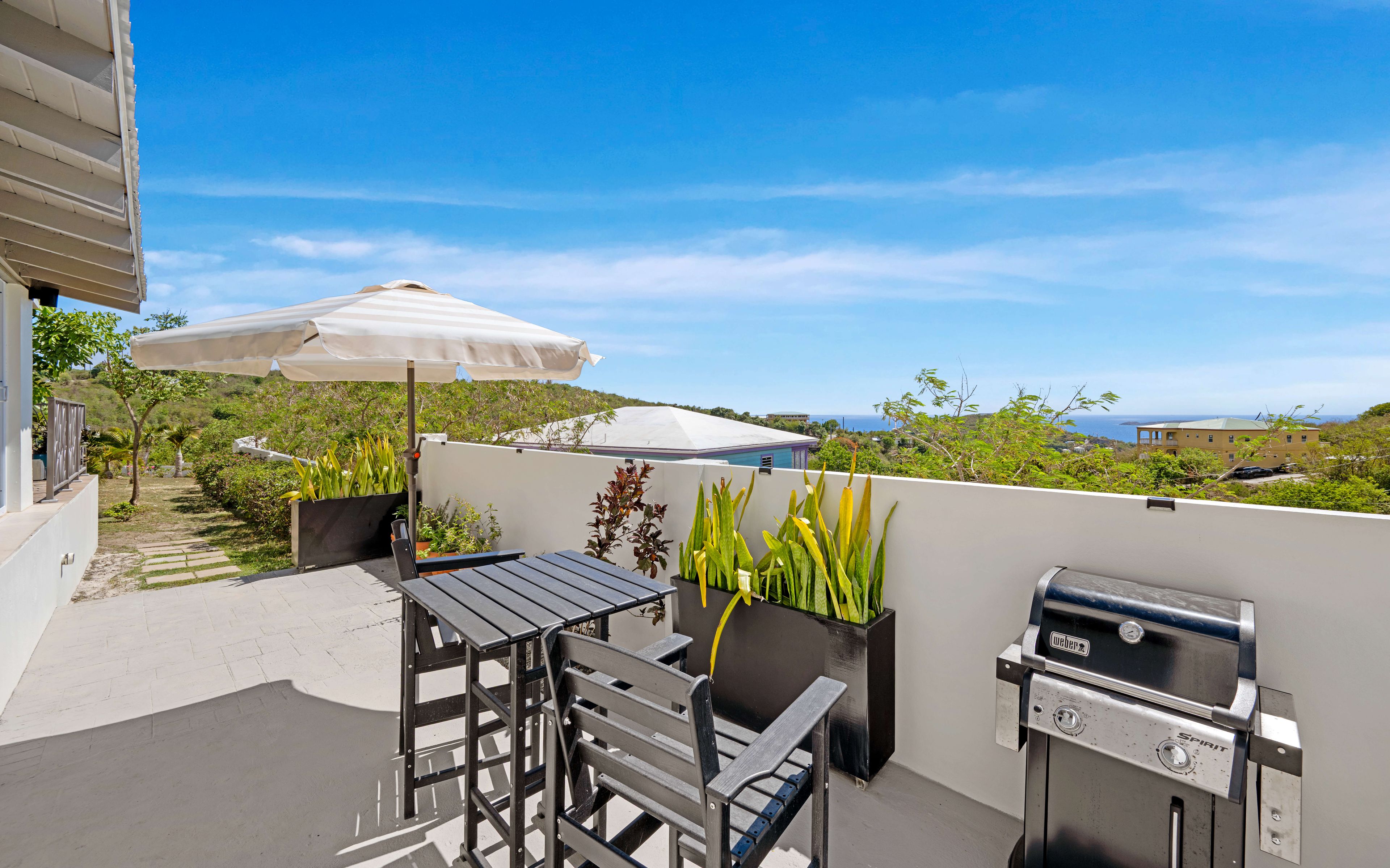 A rooftop terrace with a table, chairs, a grill, and an umbrella.
