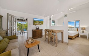 Amplia sala de estar con mesa de comedor, sillas, sofá y cama. Se ve una piscina y vegetación a través de una puerta abierta.