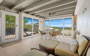 A covered patio area with a table and chairs, a wicker sofa, and a view of the sea. - Seabreeze Cottage with private pool and sunset view (Cruz Bay)