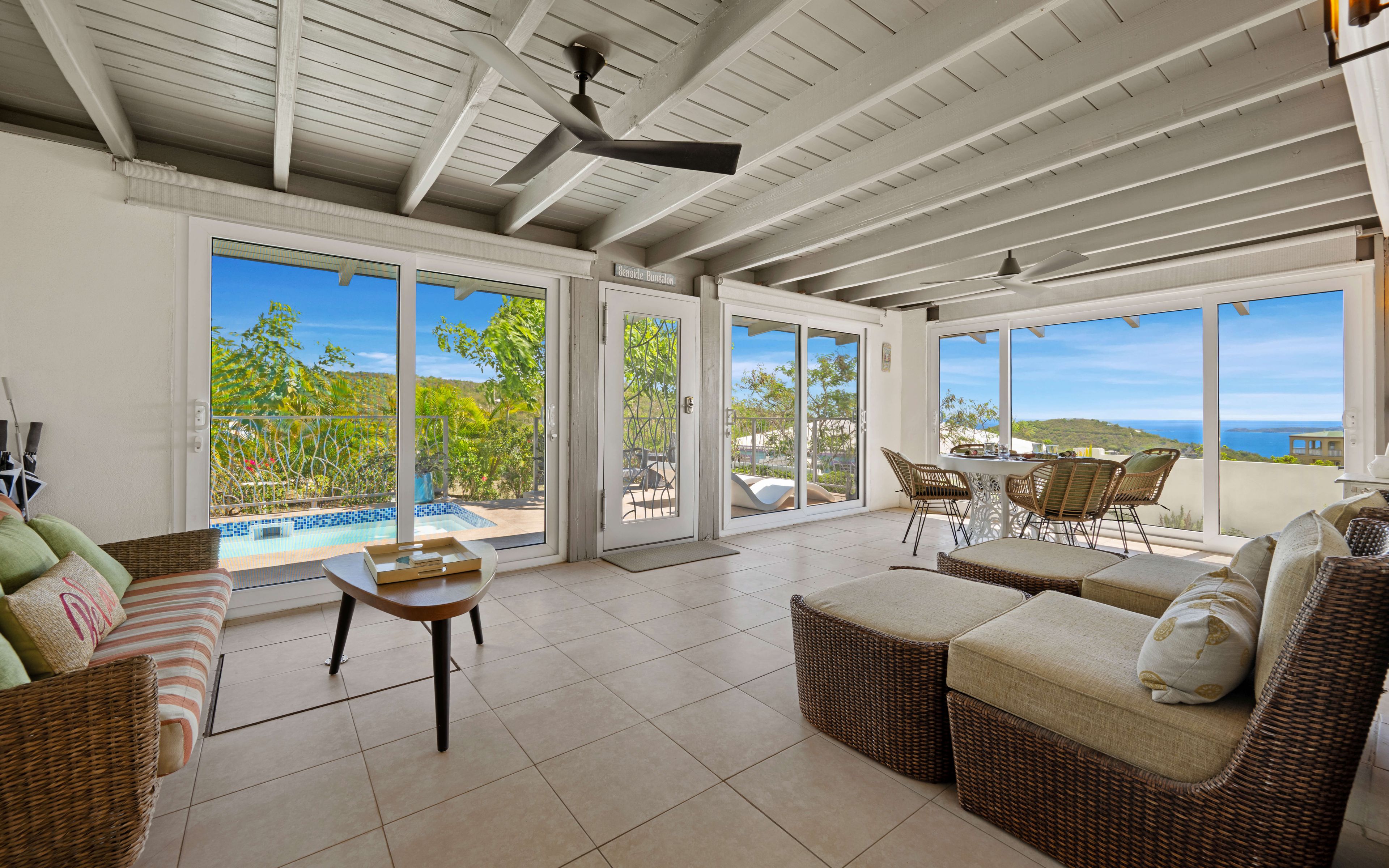 A spacious patio area with a pool, wicker furniture, and large sliding glass doors offering a view of the sea.