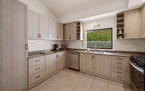 A modern kitchen with light wood cabinets, a built-in stove, and a window with a view of greenery. - Seabreeze Cottage with private pool and sunset view (Cruz Bay)