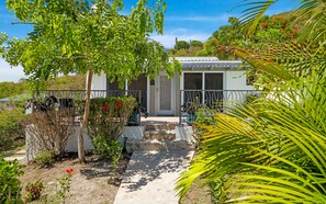 A building with a gated entrance, a pathway leading to the door, and surrounding greenery. - Seabreeze Cottage with private pool and sunset view (Cruz Bay)