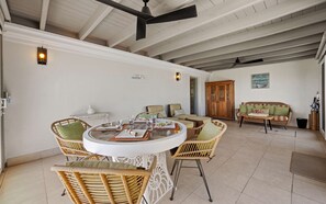 A spacious room with a round dining table surrounded by wicker chairs, a wooden cabinet, and a sofa with cushions.