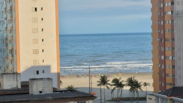 A beach view with high-rise buildings, palm trees, and a clear sky. - Residencial Texas (Praia Grande)