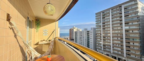 A balcony with a view of high-rise buildings, a hammock, a small table with a plant, and a decorative hanging light fixture.