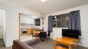 Ett kompakt bostadsutrymme med ett litet kök, en matplats, en soffa och en tv som står på ett träbord.