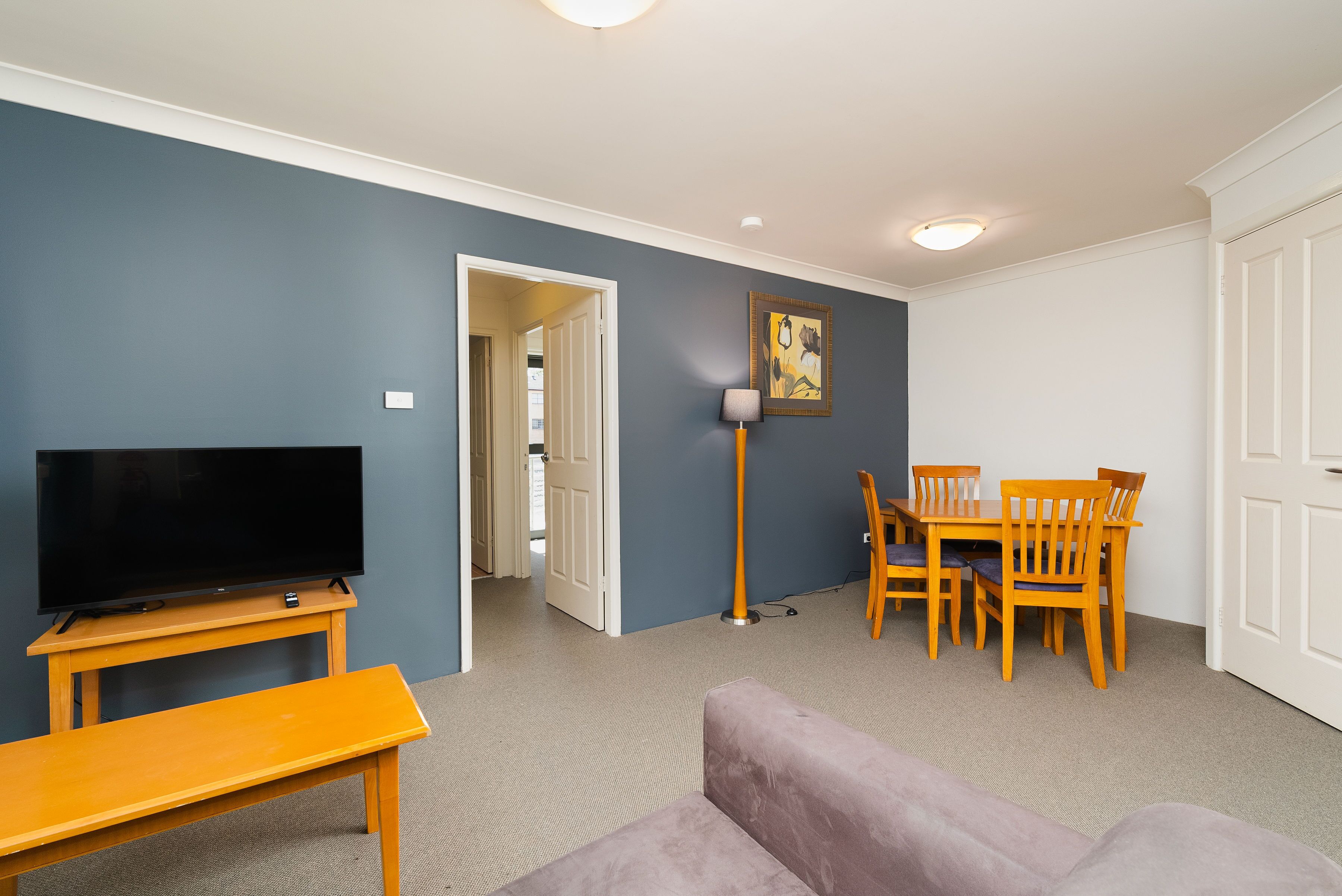 Un salon avec un téléviseur posé sur un meuble, un canapé, une table à manger avec des chaises et un tableau accroché au mur.