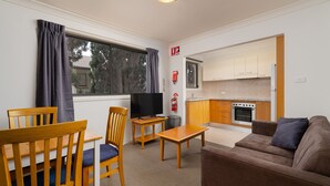 Ett kompakt bostadsutrymme med en matplats, en soffa, en TV och ett litet kök.