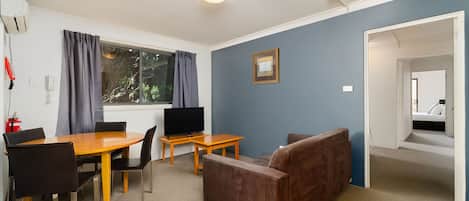 A room with a dining table, chairs, a sofa, a TV, and a window with curtains.