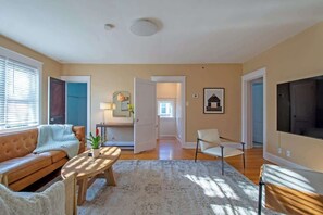 Ein Wohnzimmer mit Sofa, Couchtisch, Fernseher und einer Tür zu einem anderen Raum.